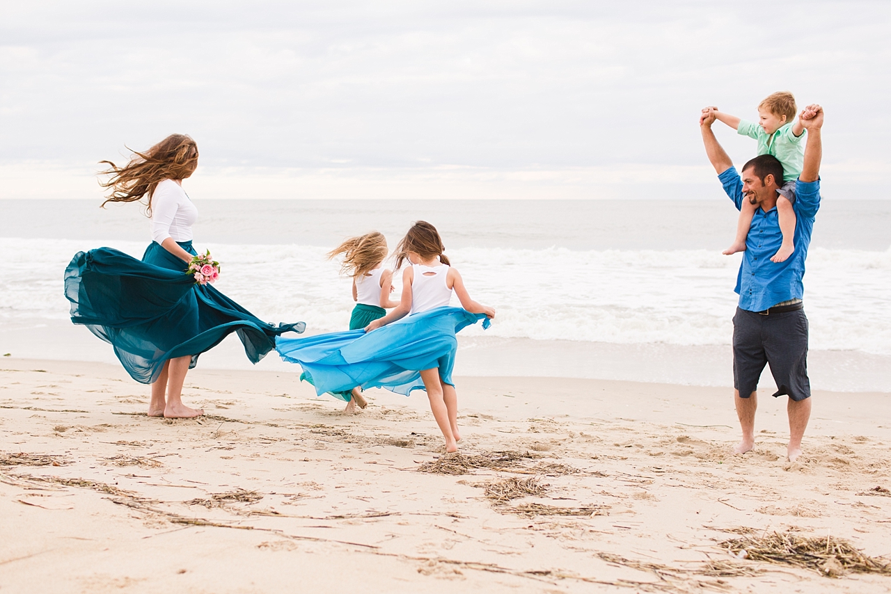 Mother and two daughter twirl their dresses while daddy and son watches at their beach family session. 