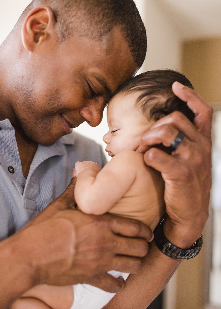 Lifestyle sessions of father smiling holds his newborn son with their foreheads touching. 