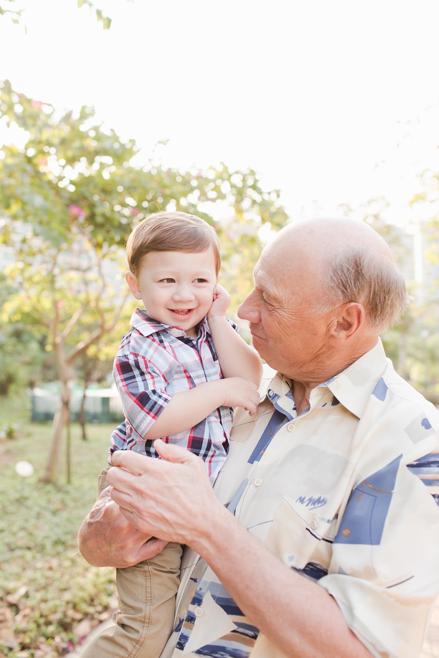 Grandfather holds his toddler grandson in an outdoor lifestyle photo session. 