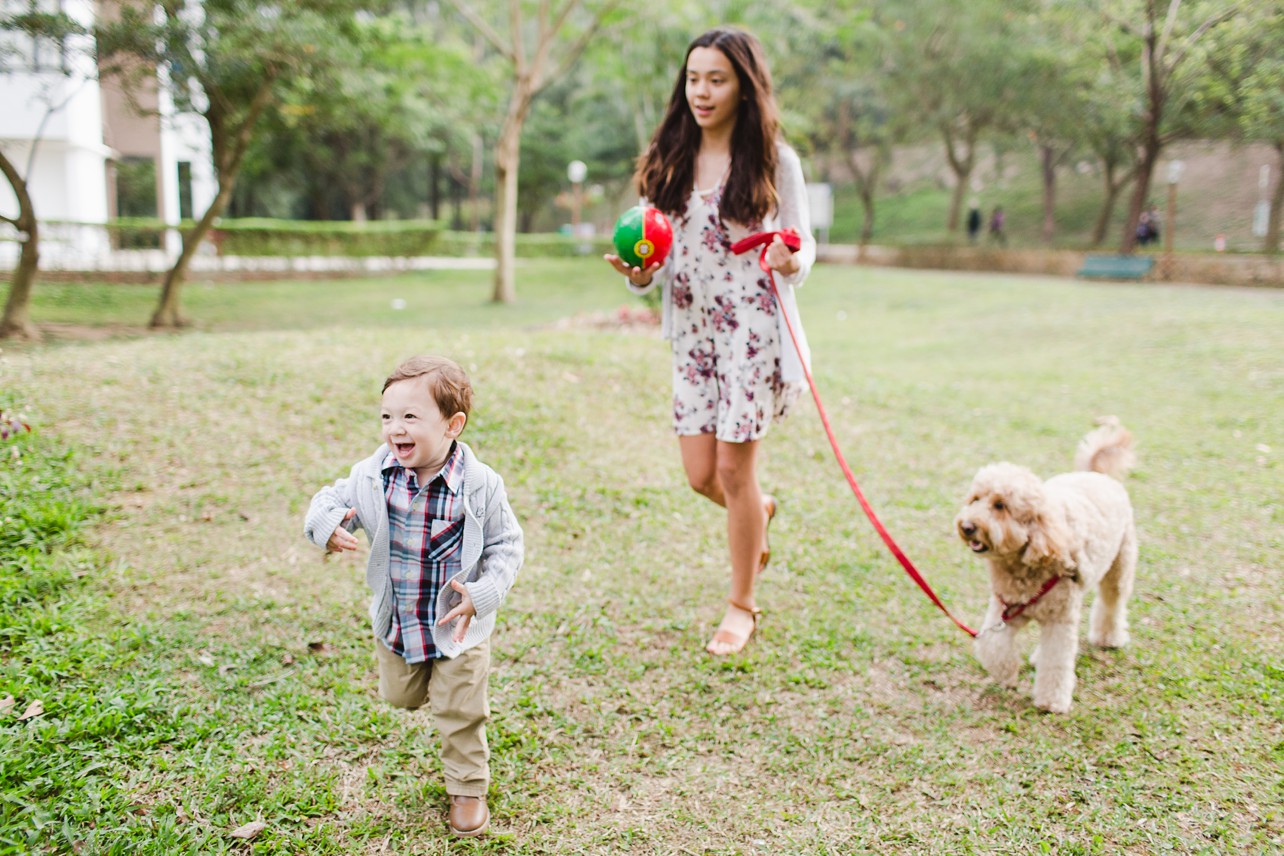A small boy runs forward while his older sister walks with their dog. 