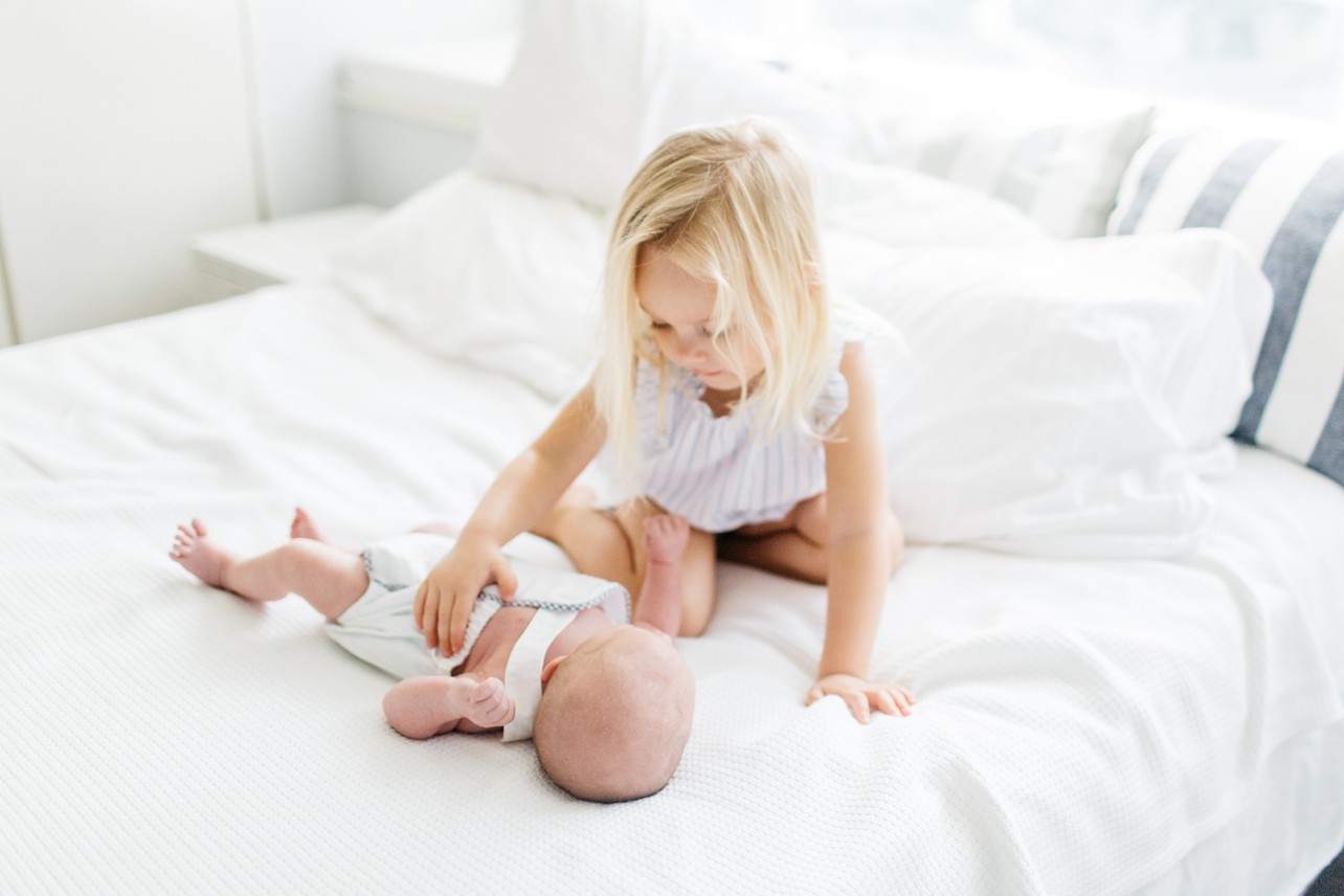 Newborn Home Lifestyle with Felix - big sister is calming a baby on the bed