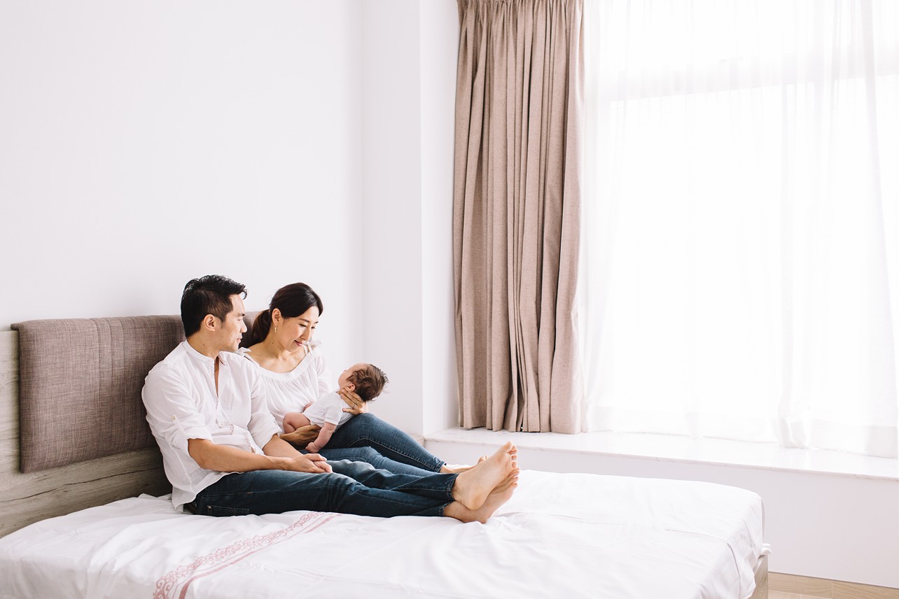 New parents sitting upright in bed looking lovingly at their baby. 