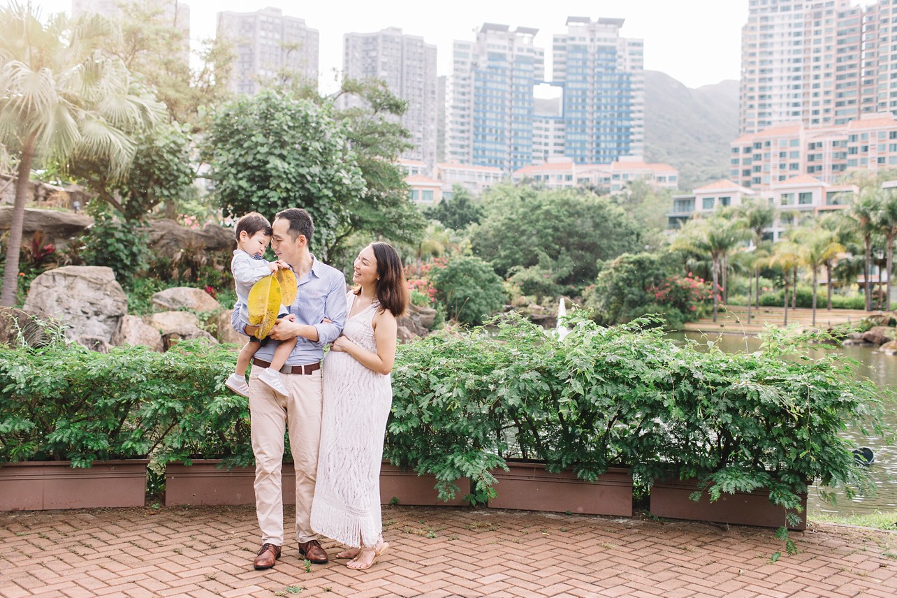 Central Park Maternity Session in Discovery Bay - family of three standing in front of the pond and a boy has a big yellow leaf