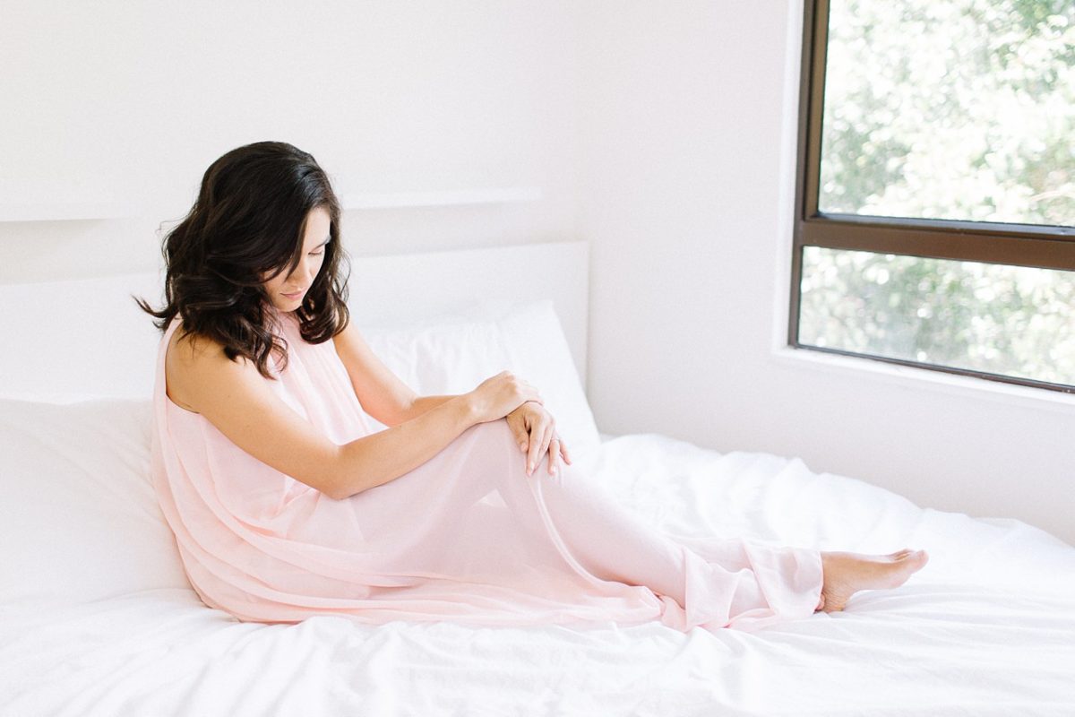 a mother in blush pink dress sitting on the bed looking down