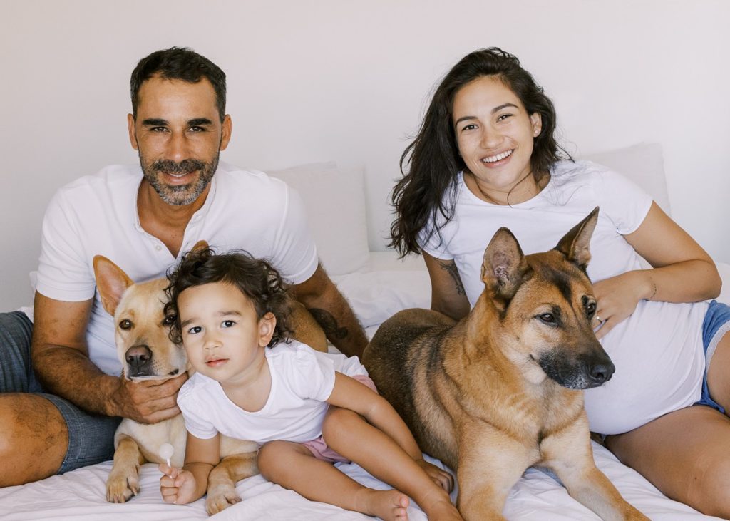 family of three with their two dogs smile at the camera for their in-home maternity session. 