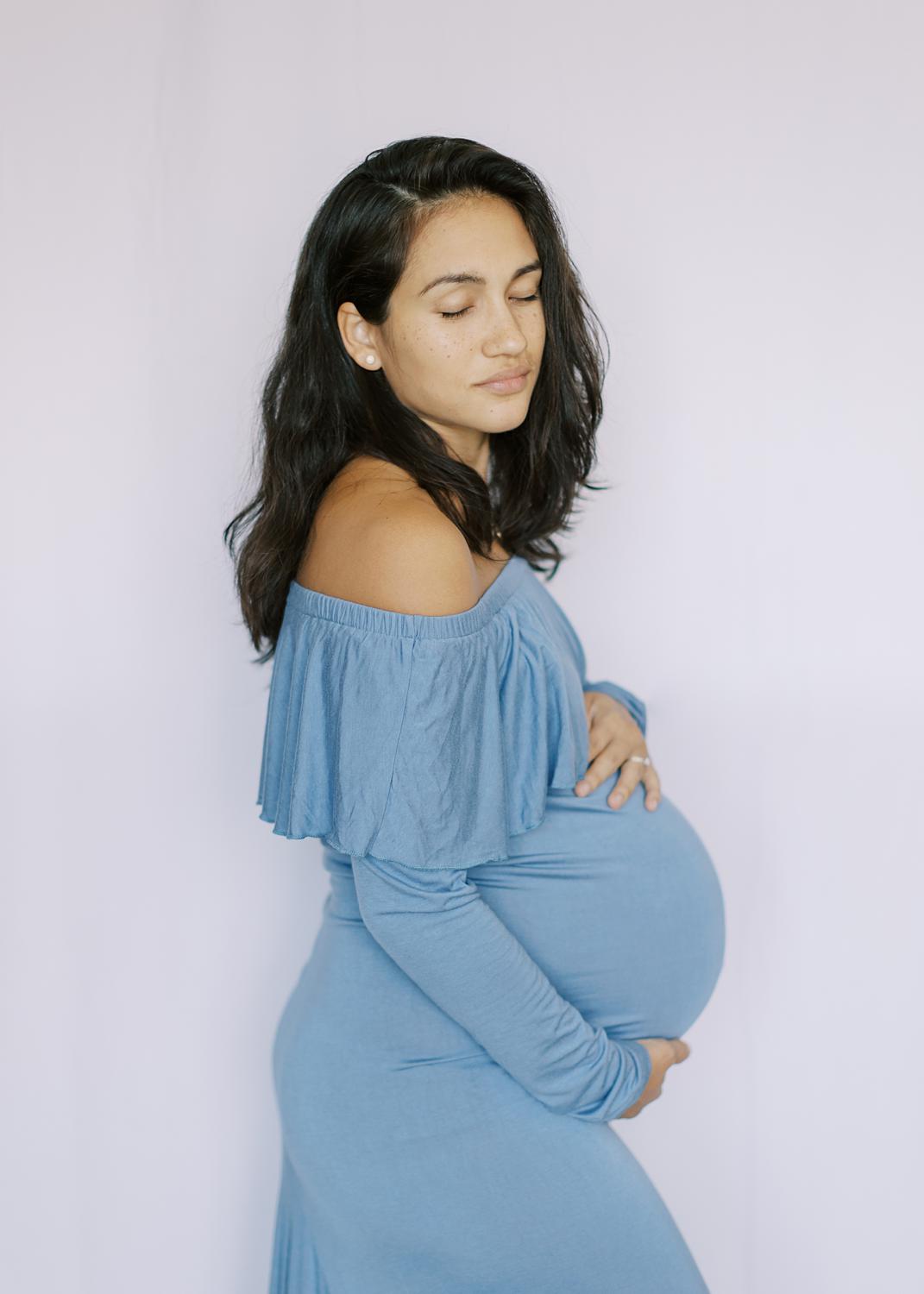pregnant mother to be in a blue maternity gown, eyes closed. 