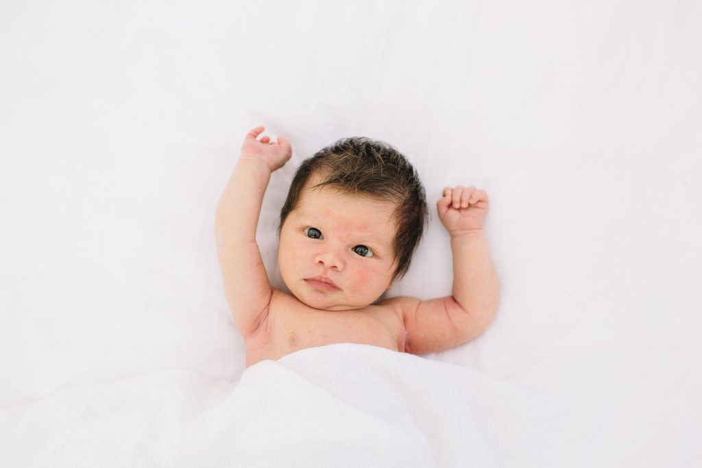 baby is awake her eyes are wide open and her arms are up on the bed