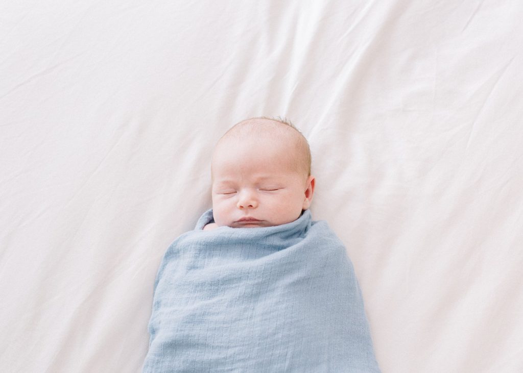 peacefully sleeping baby wrapped in blue swaddle on the white bed sheets