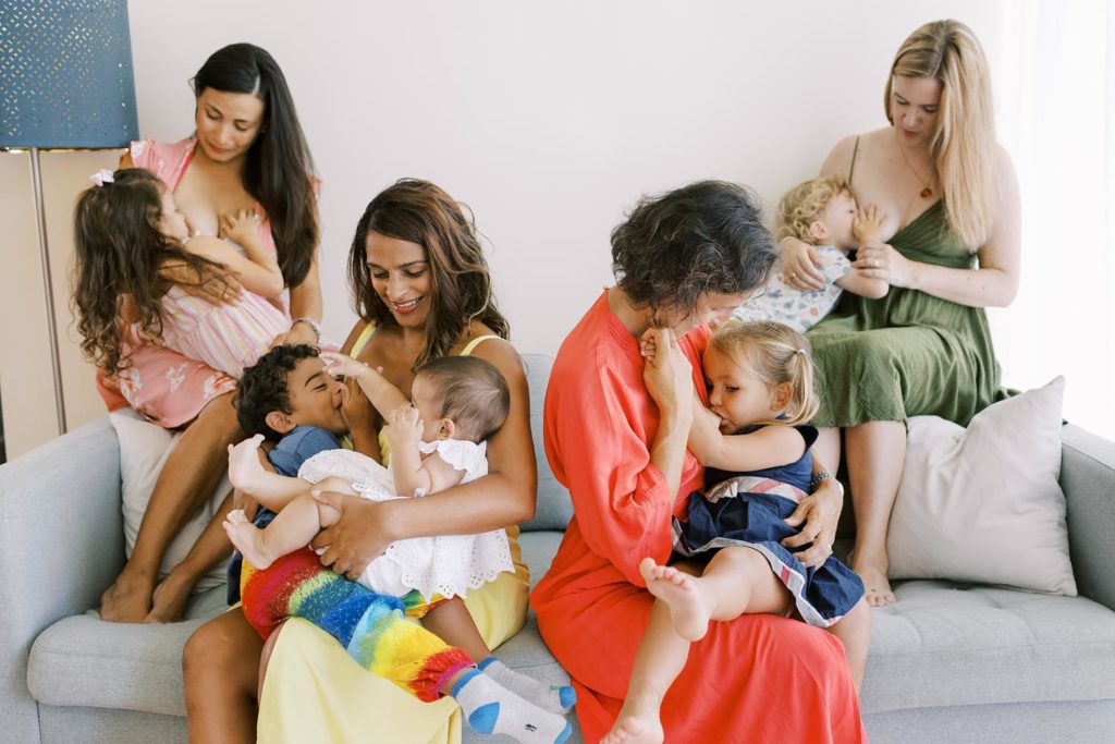 4 mothers in the colorful rainbow color dresses are breastfeeding their older kids on the couch