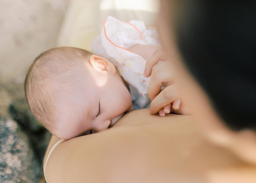 Close up of a photo of a newborn breastfeeding while mother tenderly holds child's hand. 