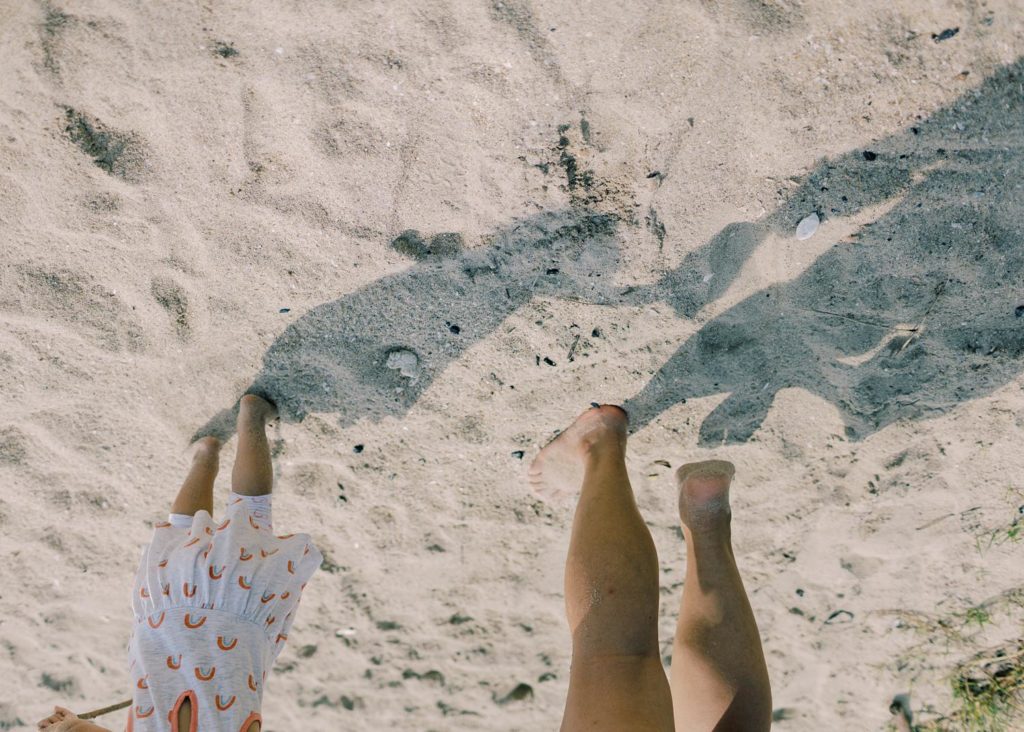 Upside down image where little girl's shadow on the sand is holding her mom's hand.