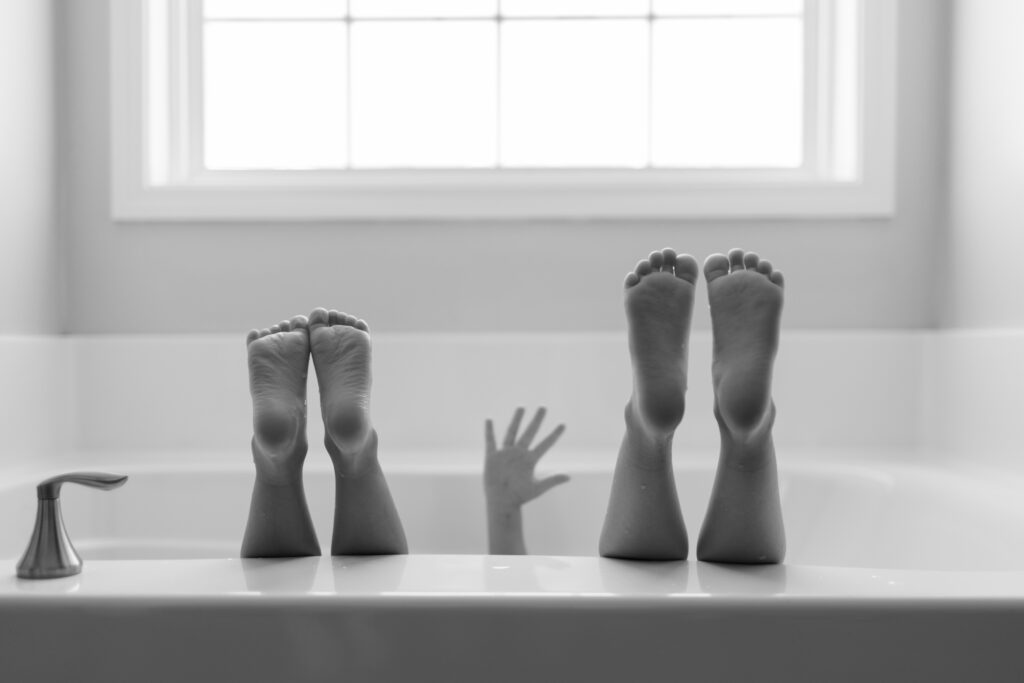Children sitting in bath with hands and feet in the air.
